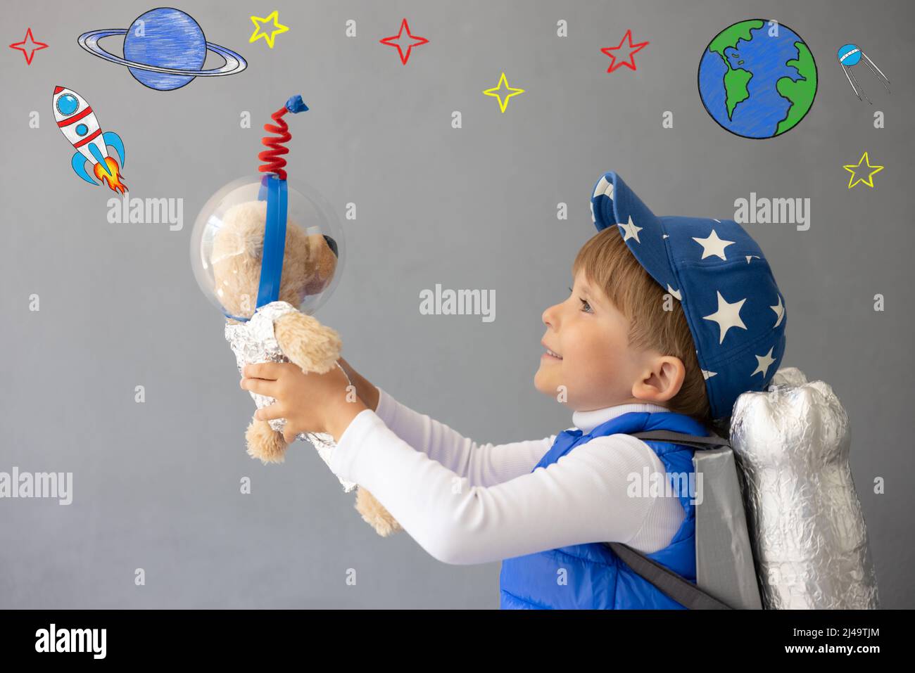 Bambino felice che gioca con il razzo giocattolo. Il bambino tiene orsacchiotto contro il fondo della parete di calcestruzzo. Ragazzo finge di essere astronauta. Imagination e bambini dr Foto Stock