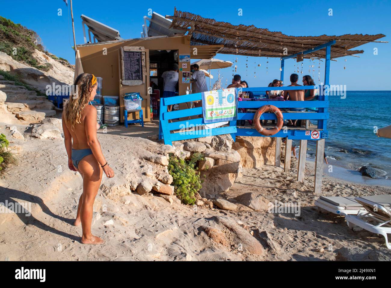 Chiringuito Bartolo bar ristorante a Playa Mitjorn spiaggia in es Caló d´es Mort cala spiaggia, i visitatori estivi si trovano su una baia fiancheggiata da scogliere rosse e r Foto Stock