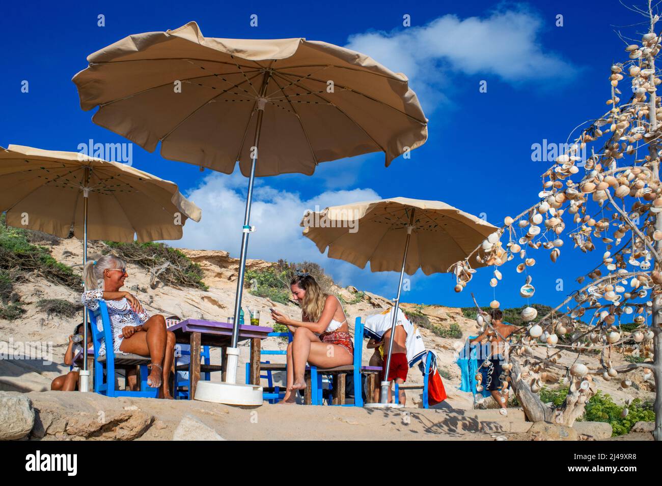 Chiringuito Bartolo bar ristorante a Playa Mitjorn spiaggia in es Caló d´es Mort cala spiaggia, i visitatori estivi si trovano su una baia fiancheggiata da scogliere rosse e r Foto Stock