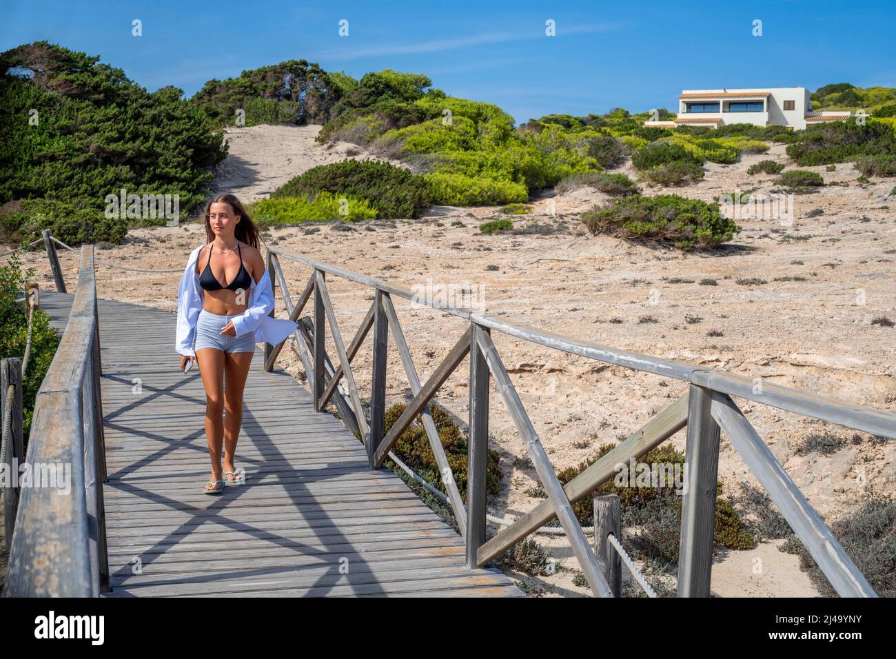 Ragazza che cammina in una passerella di legno vicino alla spiaggia di Platja Mitjorn, Formentera, isole Baleari, Spagna. Foto Stock