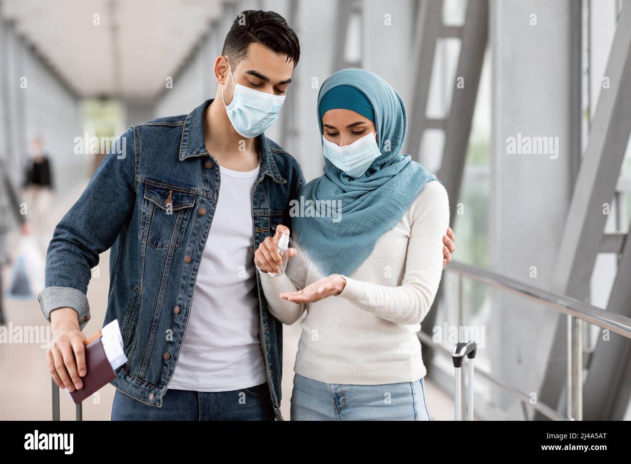 Viaggi sicuri. Giovane coppia musulmana che indossa maschera medica applicazione igienizzante in aeroporto Foto Stock