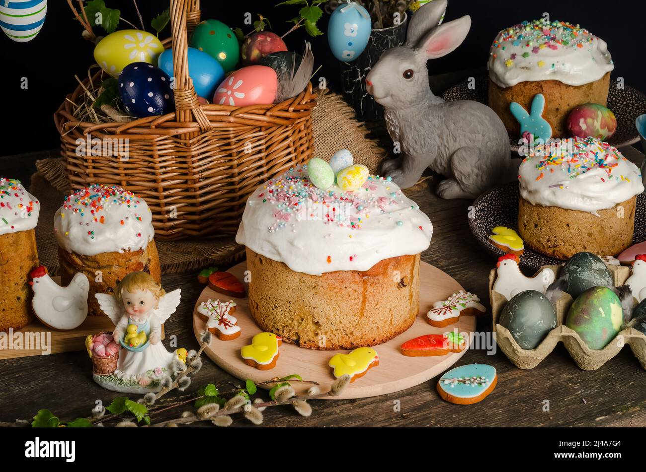 Dolci e uova di Pasqua su un tavolo pasquale festivo con salice e una statuetta di un coniglio su sfondo scuro. Foto Stock