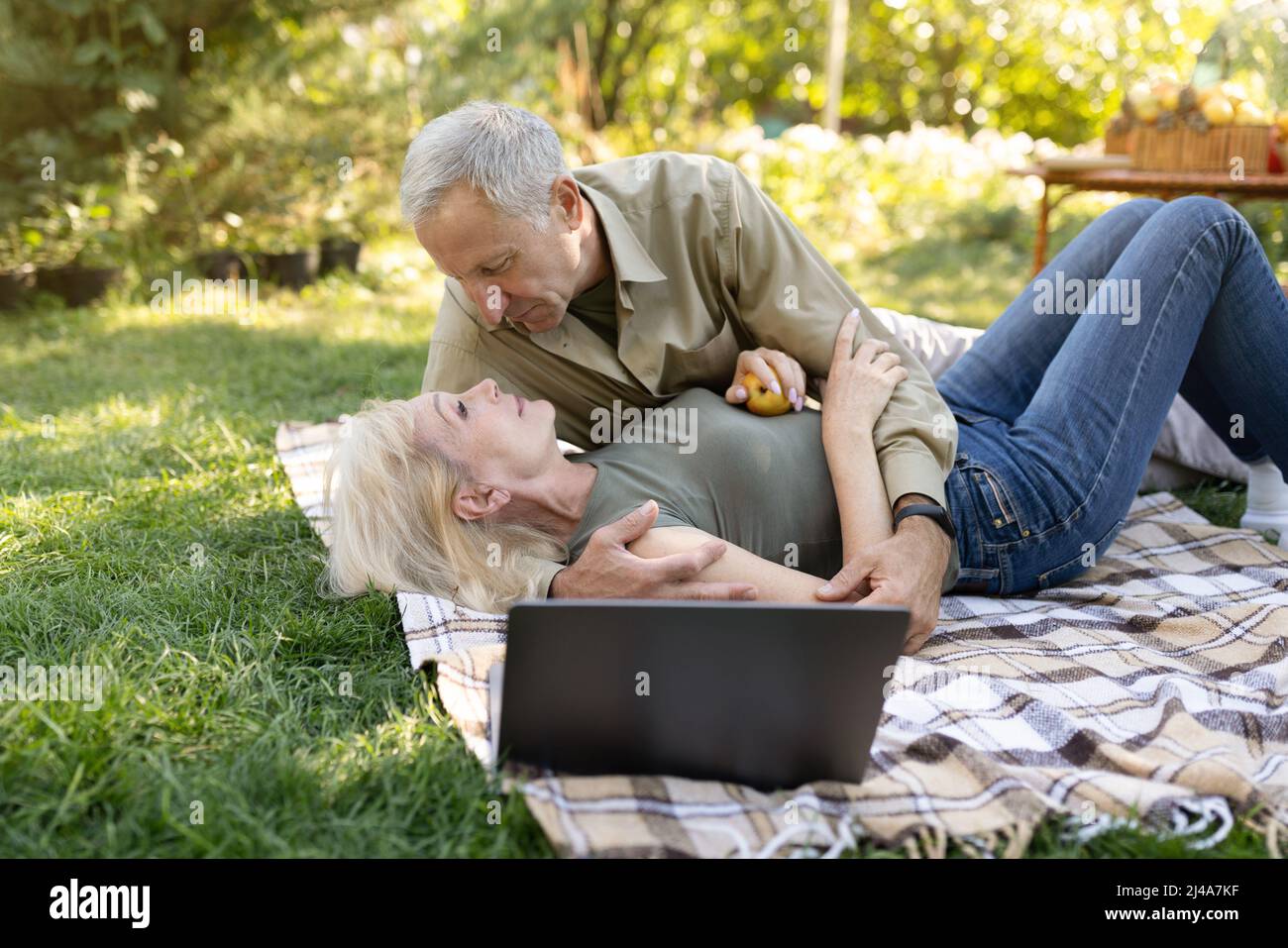 Tenera coppia sposata anziana godendosi il tempo insieme, trascorrendo la giornata all'aperto nel loro giardino, avendo picnic sul prato Foto Stock