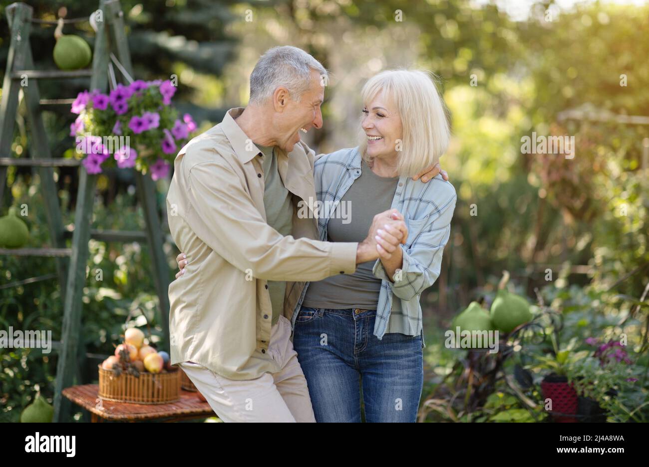 I coniugi più grandi e gioiosi ballano in giardino, tengono le mani e ridono, godendo di trascorrere il tempo insieme all'aperto Foto Stock