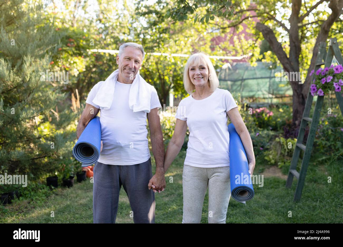 Concetto di stile di vita sano. Sposi senior sportivi felici con tappetini yoga e sorridenti alla macchina fotografica dopo aver fatto esercizio all'aperto Foto Stock