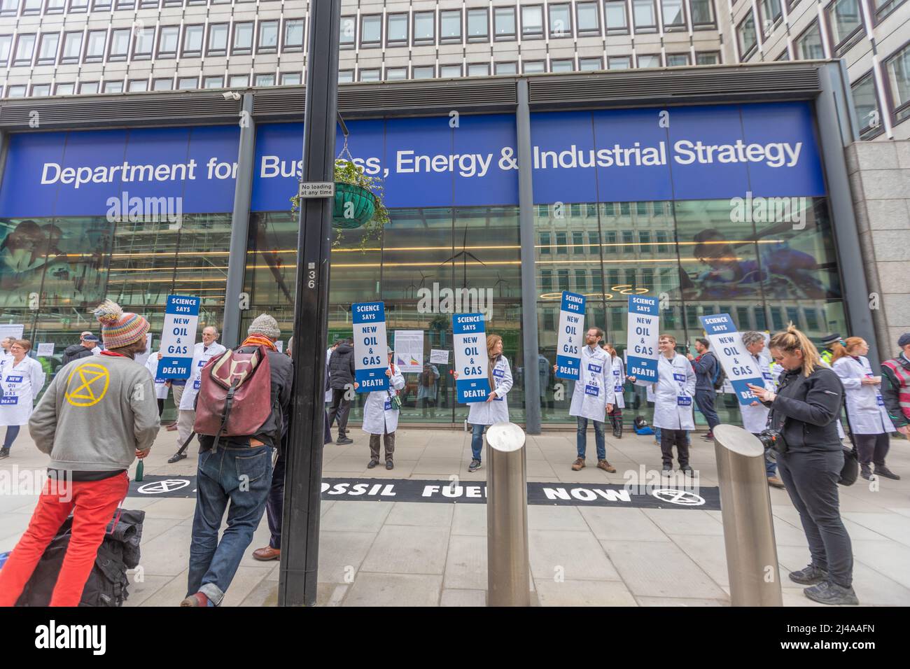 Londra, Regno Unito. 13 aprile 2022. Gli attivisti ambientalisti della ribellione per l'estinzione organizzano una protesta pacifica al di fuori del Department for Business, Energy & Industrial Strategy a Londra. I manifestanti in camici bianchi da laboratorio hanno cartelli che recano "NIENTE PETROLIO", "NIENTE GAS" e "TRANSIZIONE GIUSTA", che chiedono un'azione urgente sulla dipendenza dai combustibili fossili e una transizione energetica equa. Uno striscione nero sul terreno recita “COMBUSTIBILI FOSSILI ORA” con il simbolo della ribellione dell’estinzione. La protesta evidenzia la preoccupazione dell'opinione pubblica per la politica climatica e la strategia energetica. Penelope Barritt/Alamy Live News Foto Stock