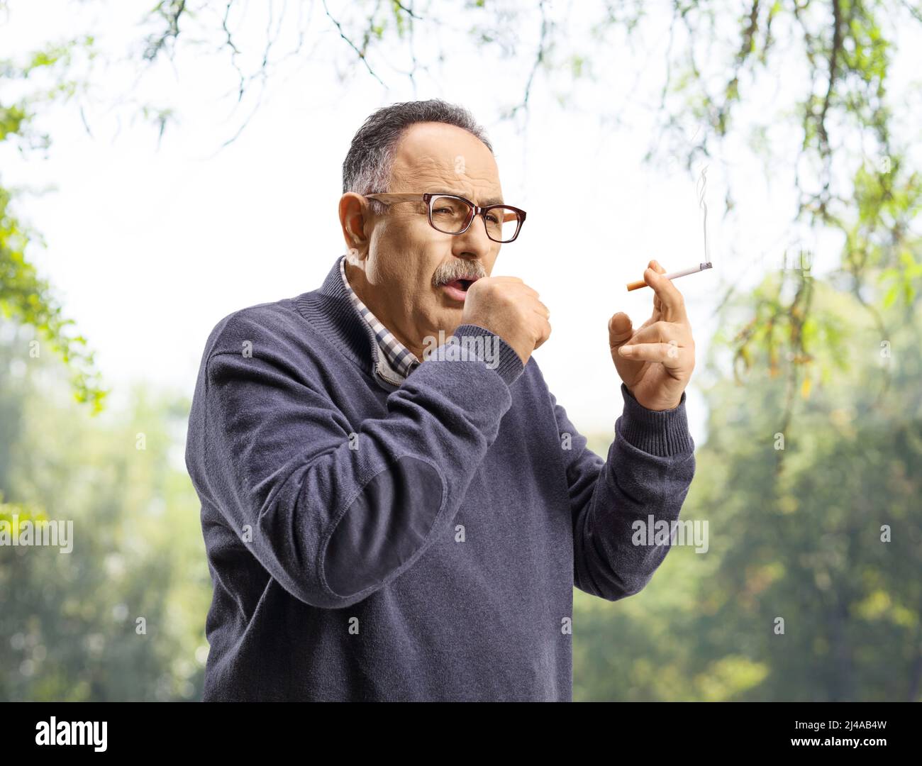 Uomo maturo che fuma e tossisce all'aperto in un parco Foto Stock