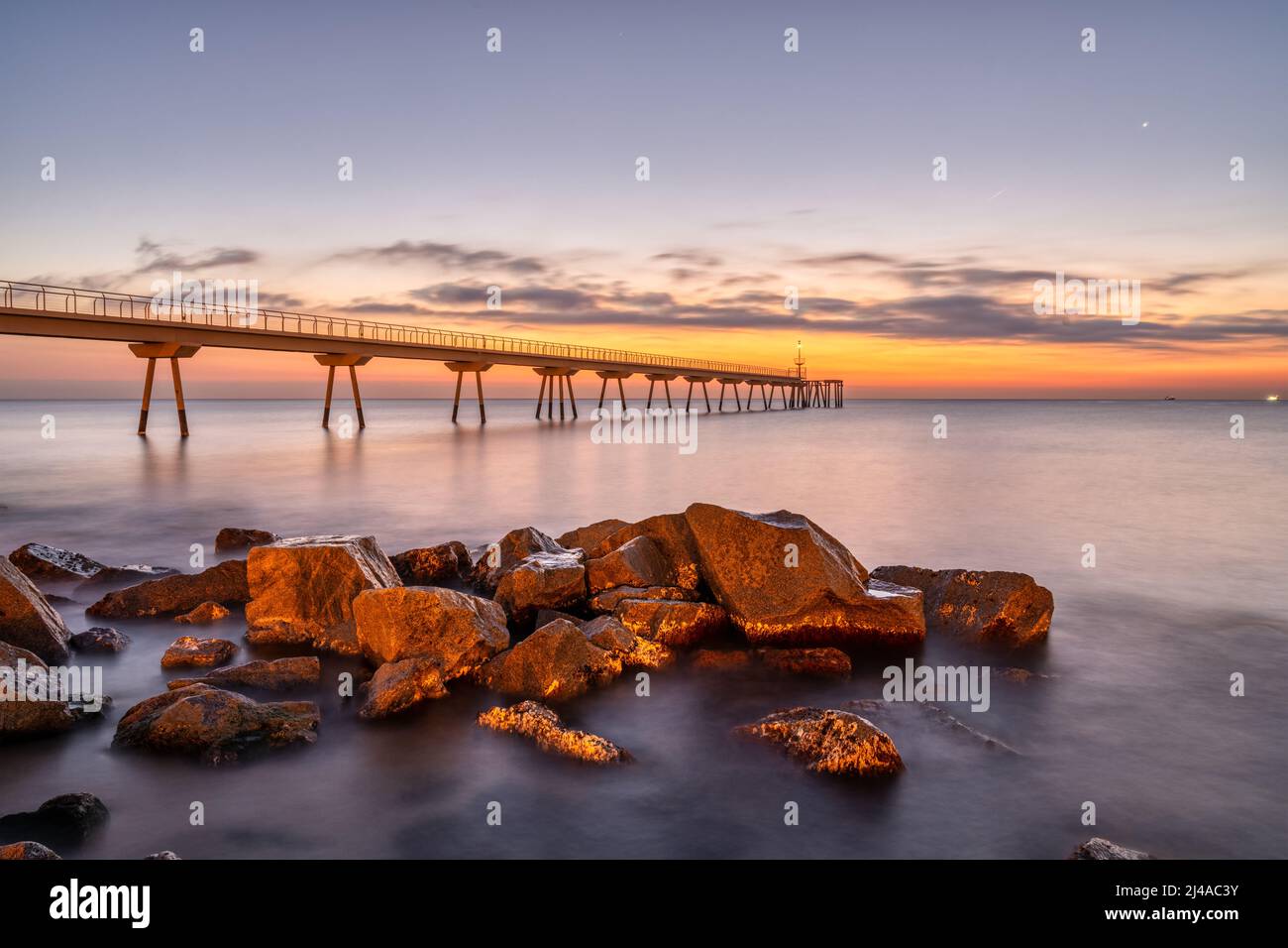 Il molo marino di Badalona in Spagna con alcune rocce prima dell'alba Foto Stock