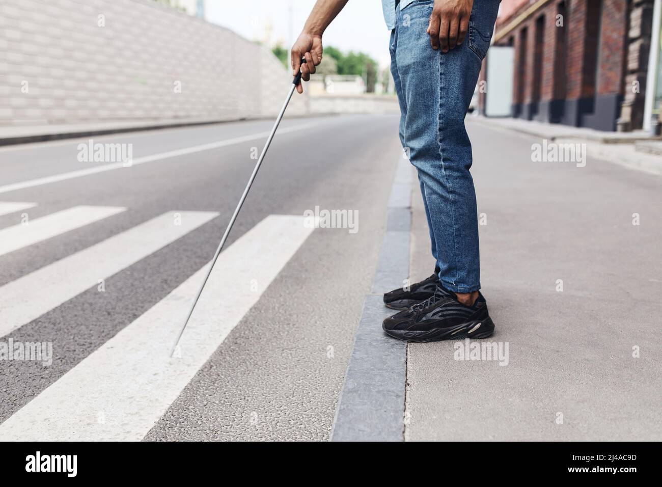 Vista ritagliata del giovane ragazzo nero con disabilità visiva in piedi sulla strada, utilizzando bastone a piedi nel centro della città, spazio copia Foto Stock