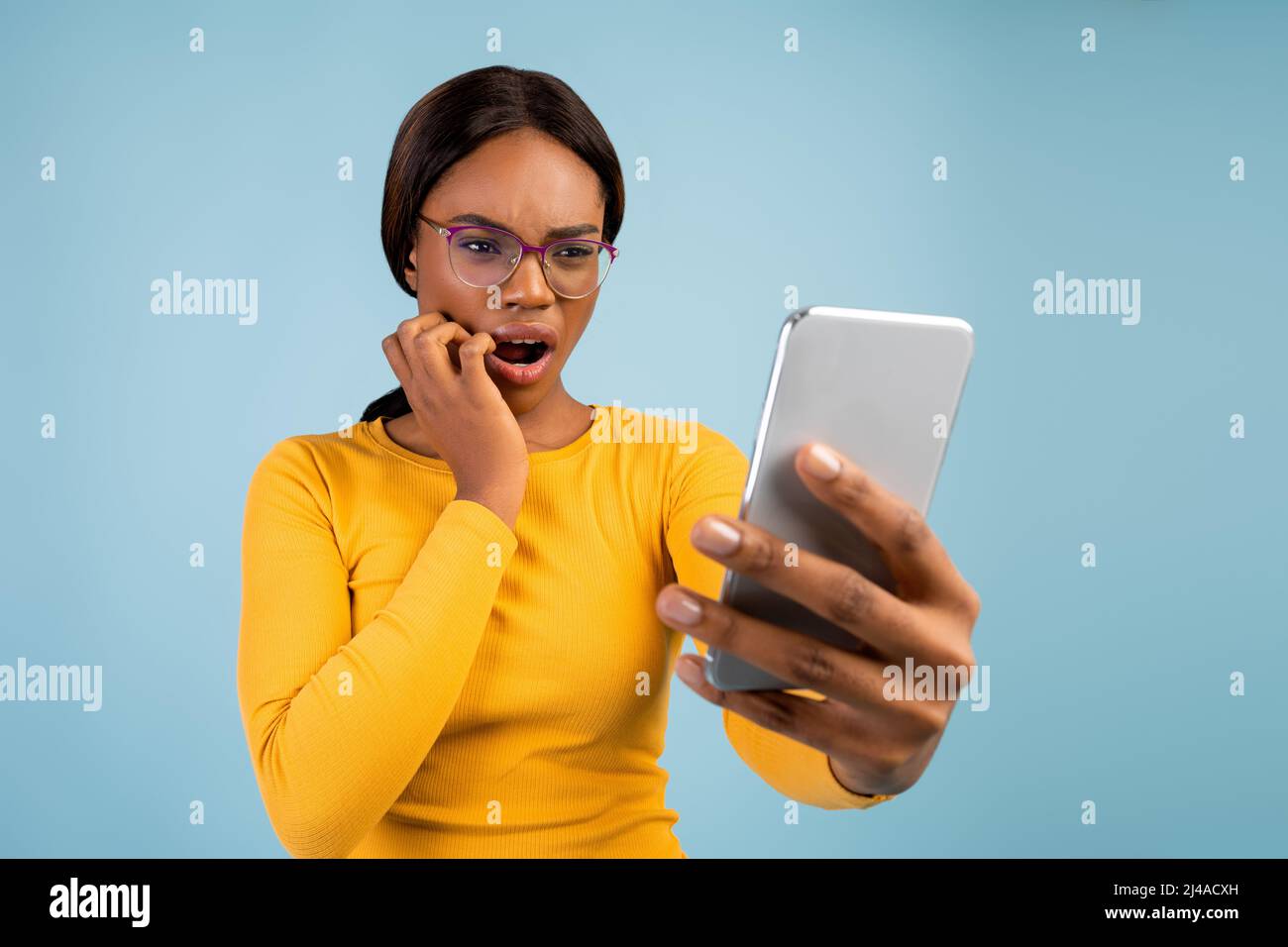 Scioccata donna millenaria afroamericana in occhiali con bocca aperta legge il messaggio al telefono Foto Stock