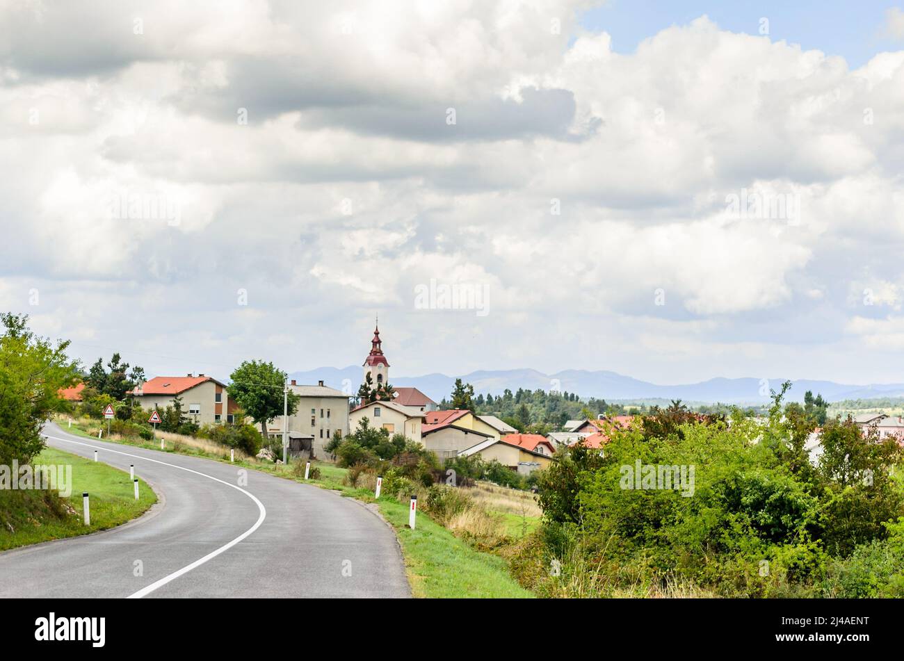 Old National Winding Road nella campagna slovena. Passando attraverso un villaggio tradizionale con cottage e una chiesa in un ambiente naturale Foto Stock