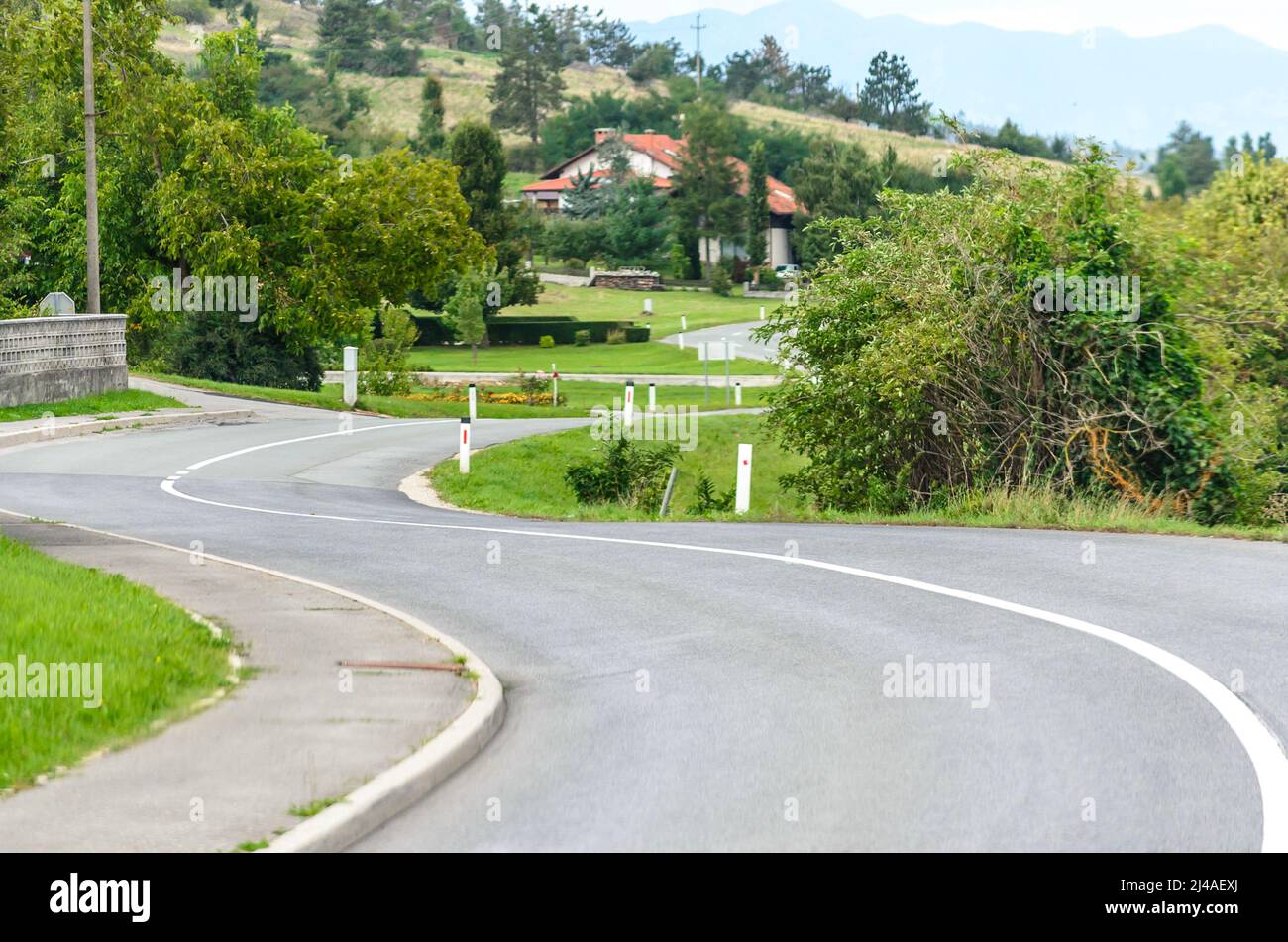 Old National Winding Road nella campagna slovena. Passando attraverso un ambiente naturale con erba verde, alberi e cottage tradizionali Foto Stock