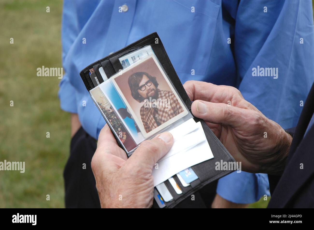L uomo a una riunione di famiglia con i parenti guardando 60s foto del figlio ancora in portafoglio dopo 40 anni Foto Stock