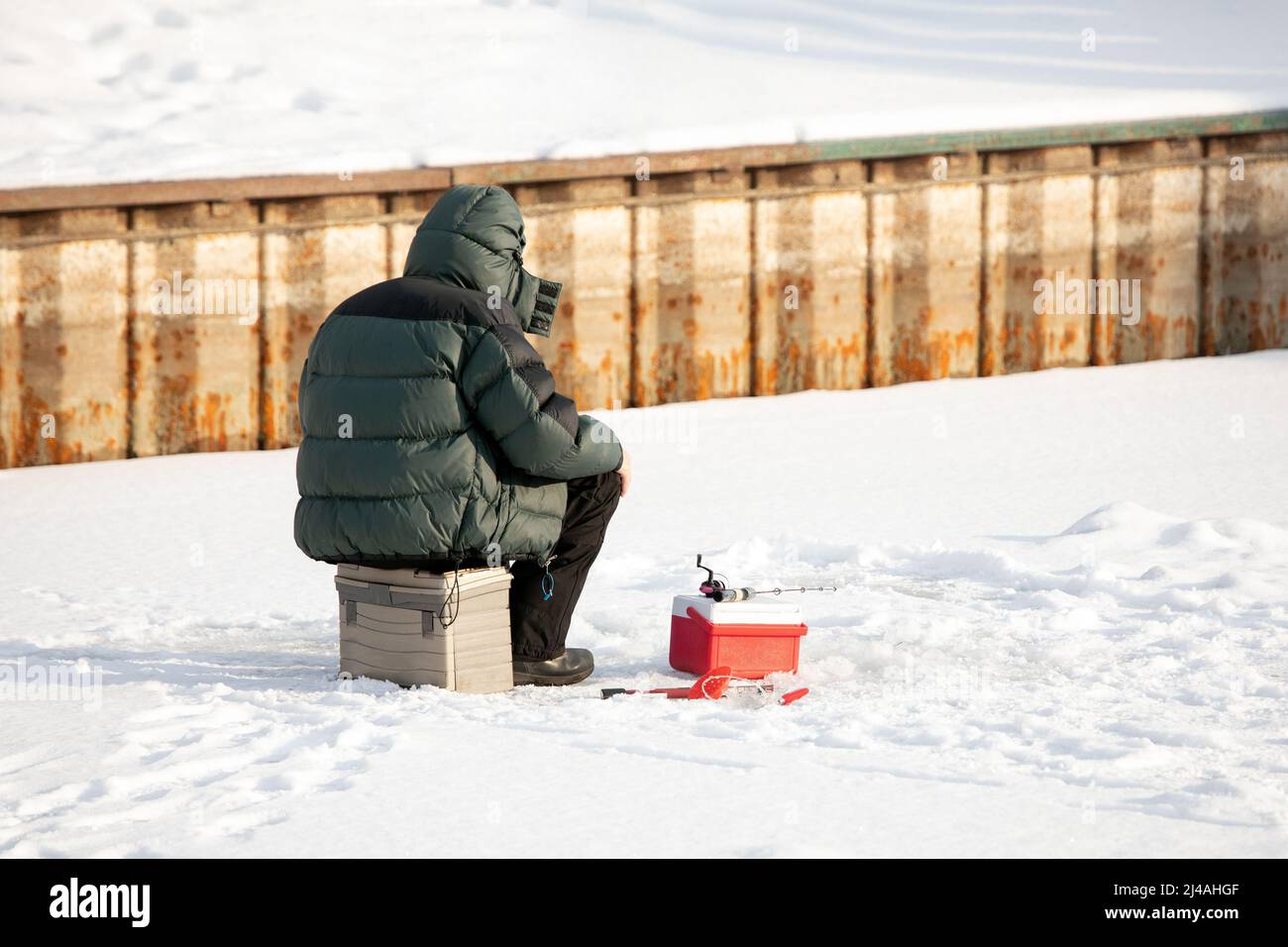 Un pescatore di ghiaccio sul lago con il suo equipaggiamento Foto Stock
