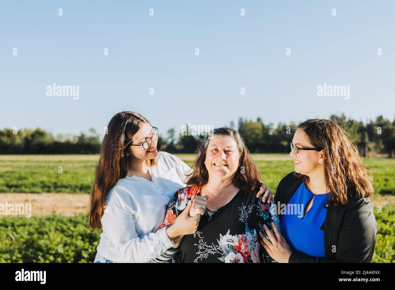 Famiglia femminile sorridente e abbracciata in campo in un pomeriggio di sole. Giornata delle madri. Foto Stock