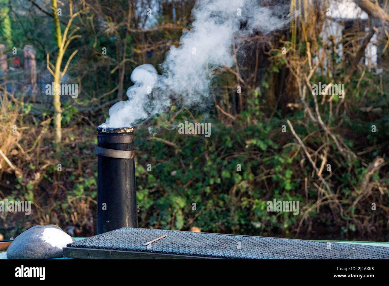Una pila di fumo su una barca stretta che mantiene caldo l’equipaggio in un giorno d’inverno, accanto ad un moderno pannello solare il canale Lee e Stort a Sawbridgeworth Foto Stock