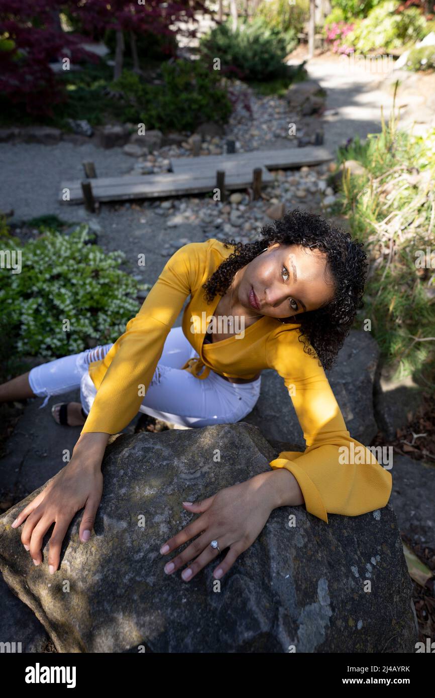 Bella giovane donna nera seduta su rocce in un giardino giapponese Foto Stock