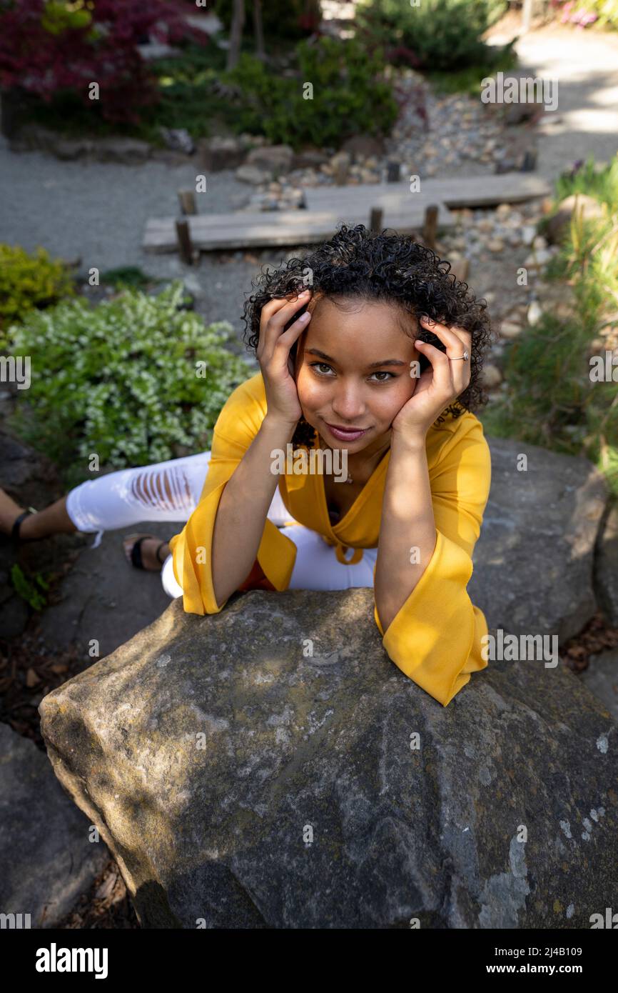 Bella giovane donna nera seduta su rocce in un giardino giapponese Foto Stock