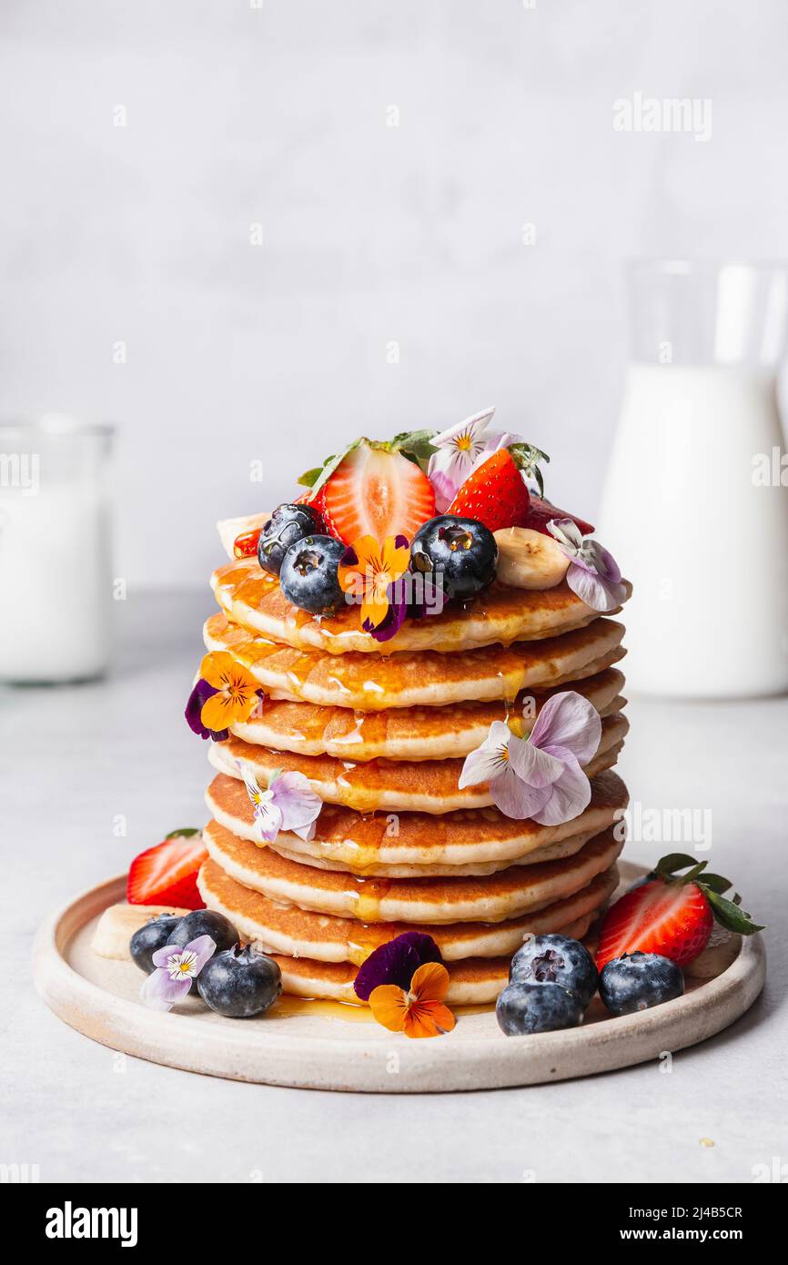 Frittelle, servite con fragole, mirtilli, banana, fiori commestibili e sciroppo. Foto Stock