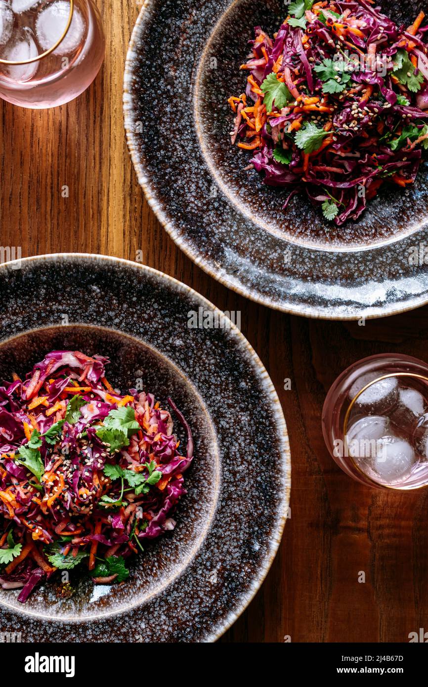 Due piatti con insalata di cavolo rosso, bicchiere, vista dall'alto, su sfondo di legno Foto Stock