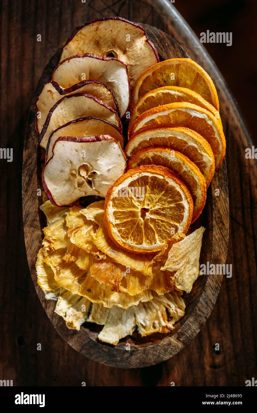 Vista dall'alto di sottili fette di frutta secca, ananas, mela e arancia, su un piccolo vassoio di legno, su un tavolo di legno Foto Stock