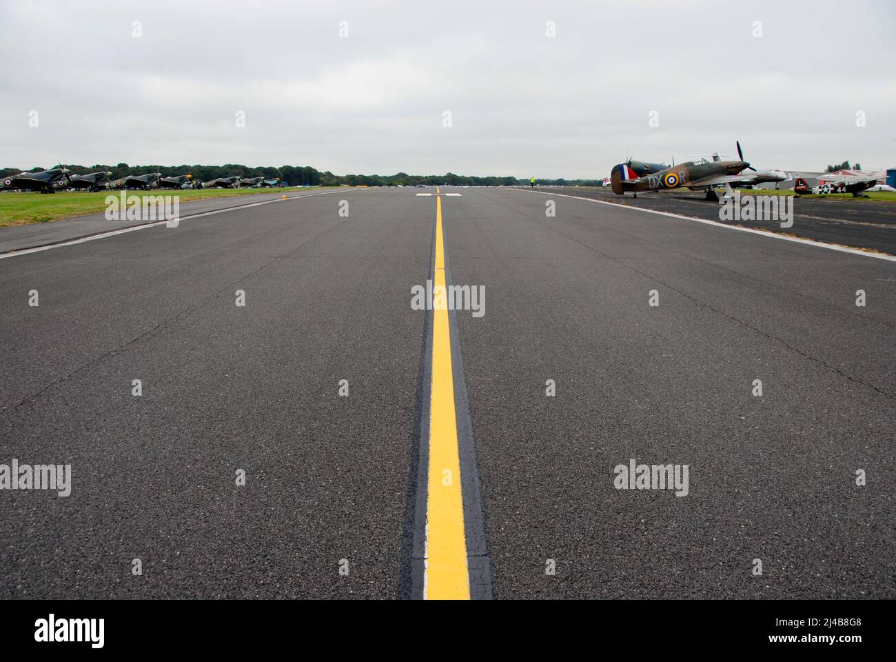 Linea gialla centrale sulla linea di taxi del campo aereo con gli aerei della seconda guerra mondiale parcheggiati da entrambi i lati all'esposizione aerea, Biggin Hill, Kent, Inghilterra Foto Stock