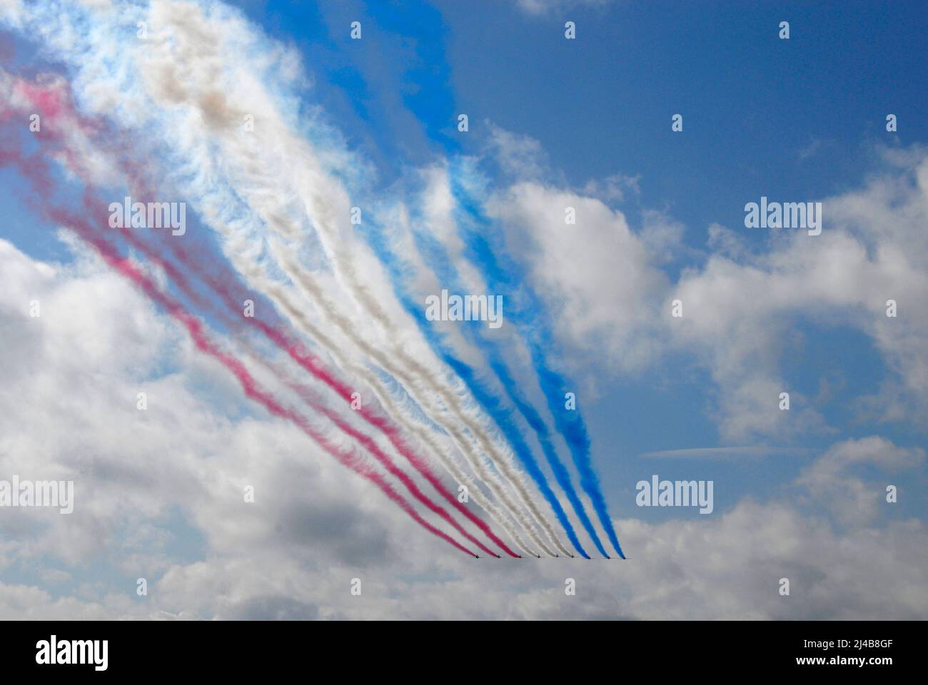 La squadra aerobatica RAF Red Arrows vola in lontananza lasciando dietro di loro sentieri di fumo rosso, bianco e blu Foto Stock
