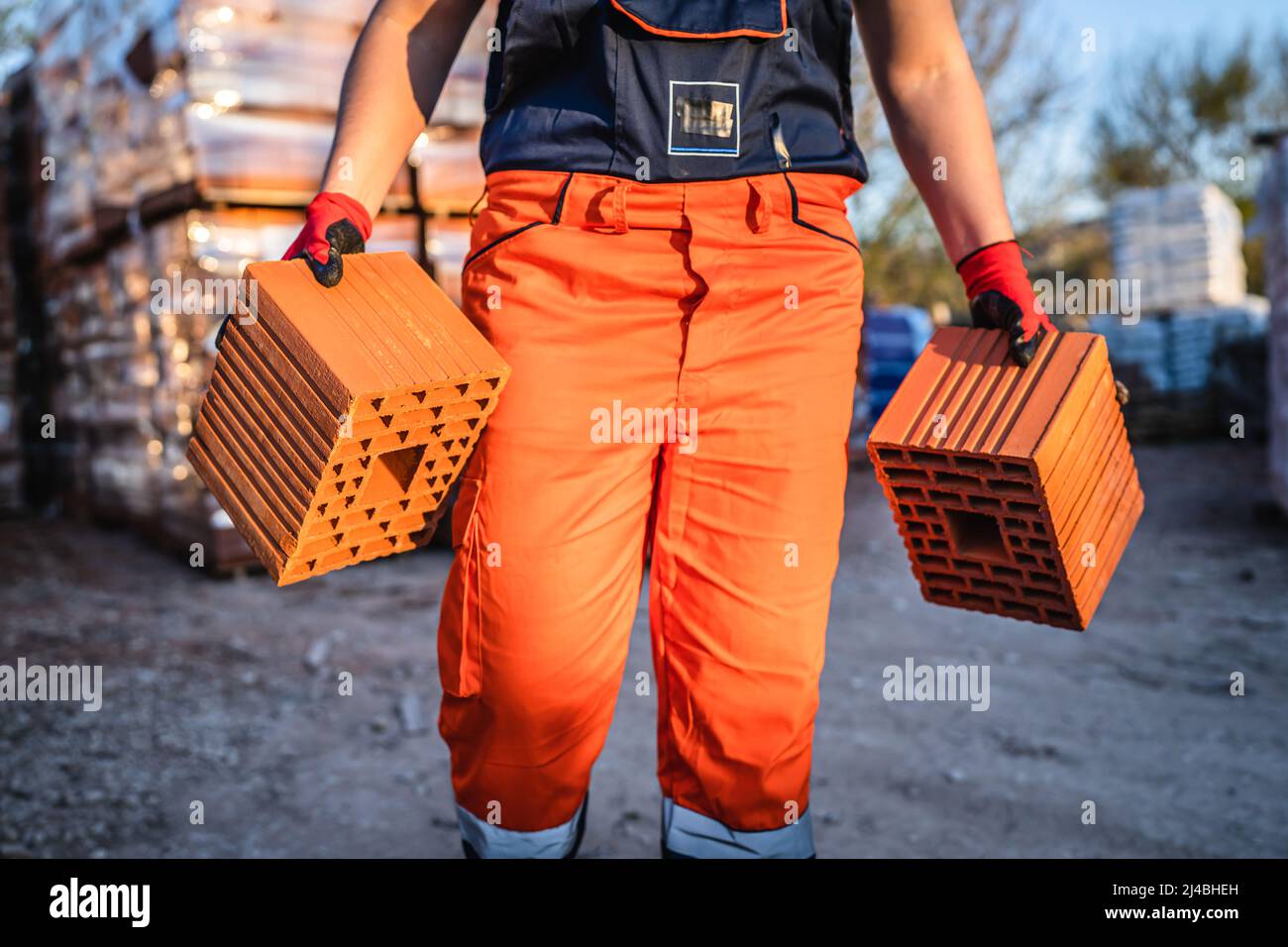 Primo piano sulle mani e nella parte centrale di un lavoratore di costruzione sconosciuto che prende blocchi di argilla cava arancione ar magazzino o cantiere di costruzione in estate soleggiata Foto Stock