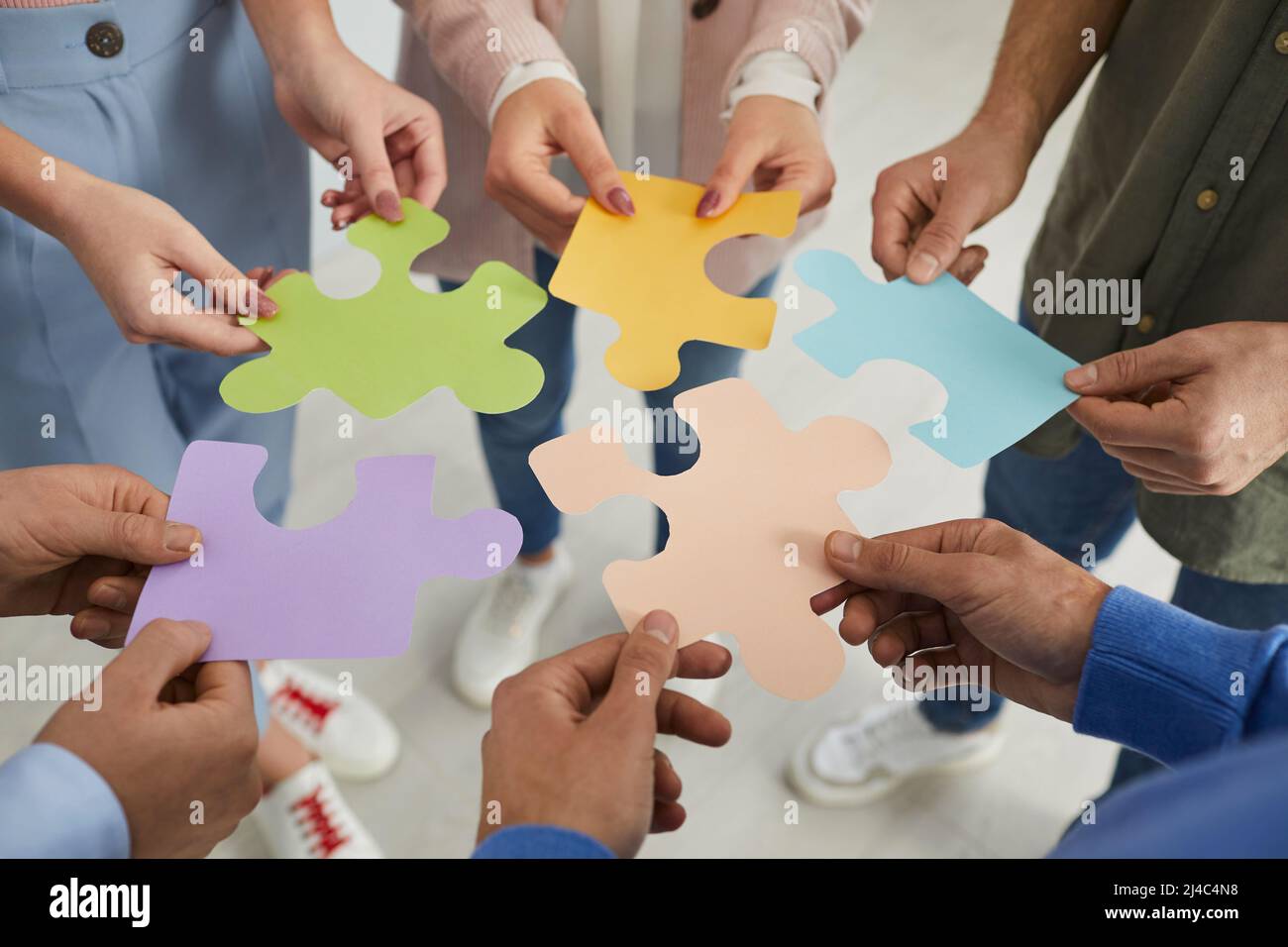 Primo piano di mani maschili e femminili che tengono e piegano insieme pezzi colorati di puzzle. Foto Stock
