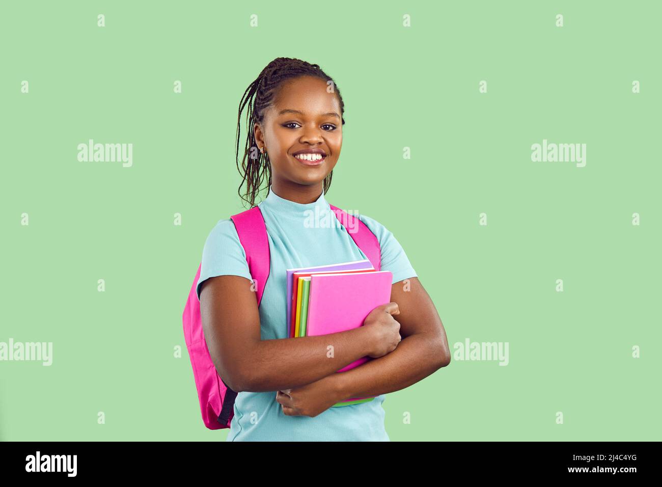 Studentessa sorridente con pelle scura e zaino e libri di testo su sfondo verde chiaro. Foto Stock