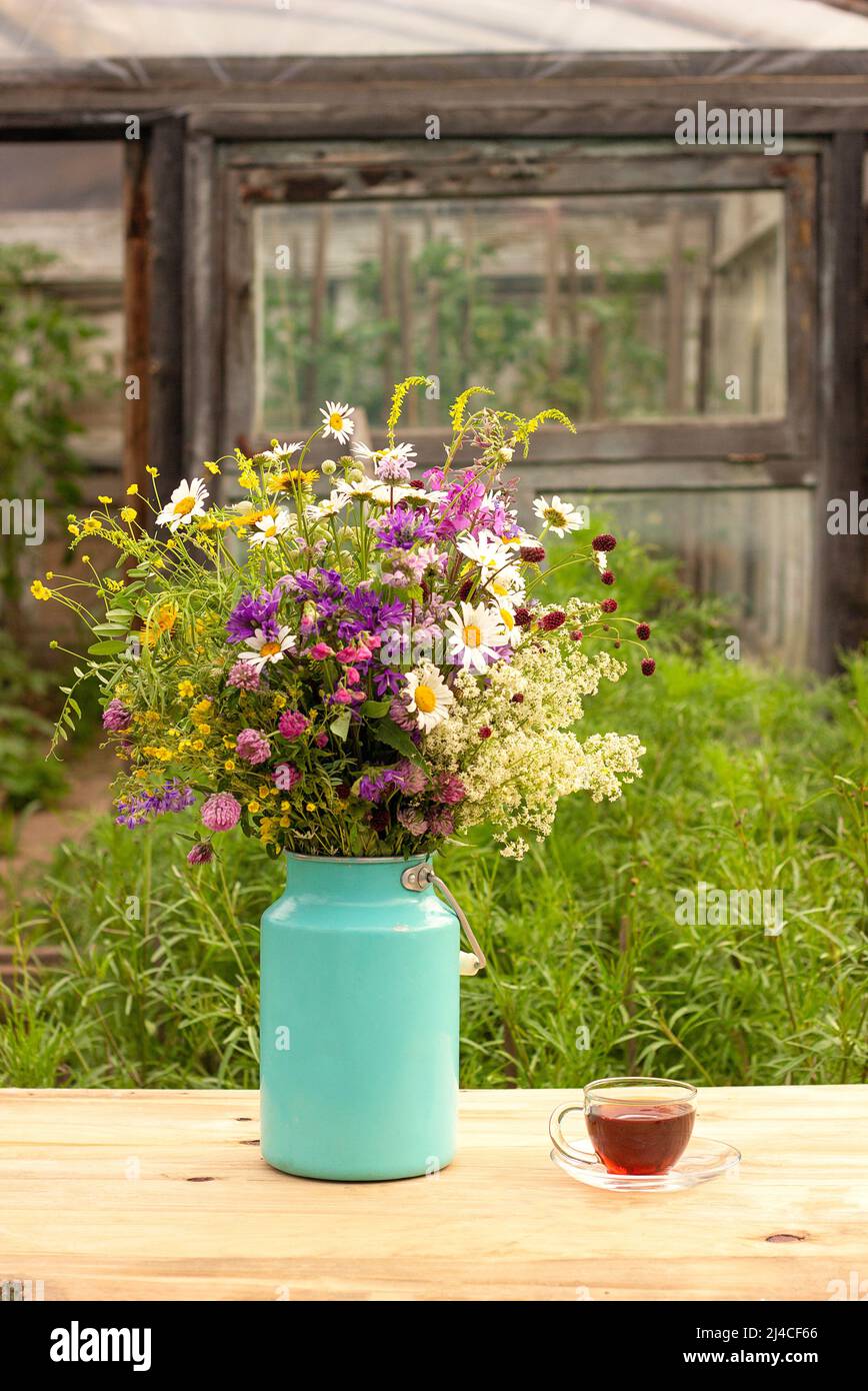 Bouquet di fiori luminosi in lattina vaso e tazza di tè in estate giorno. Foto Stock