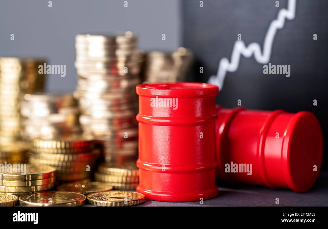 Barili rossi, pile di denaro e una curva crescente che simboleggia i prezzi elevati del carburante Foto Stock