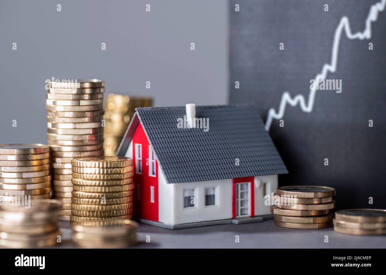 Casa con pile di denaro e una curva crescente simboleggia l'aumento dei prezzi immobiliari Foto Stock