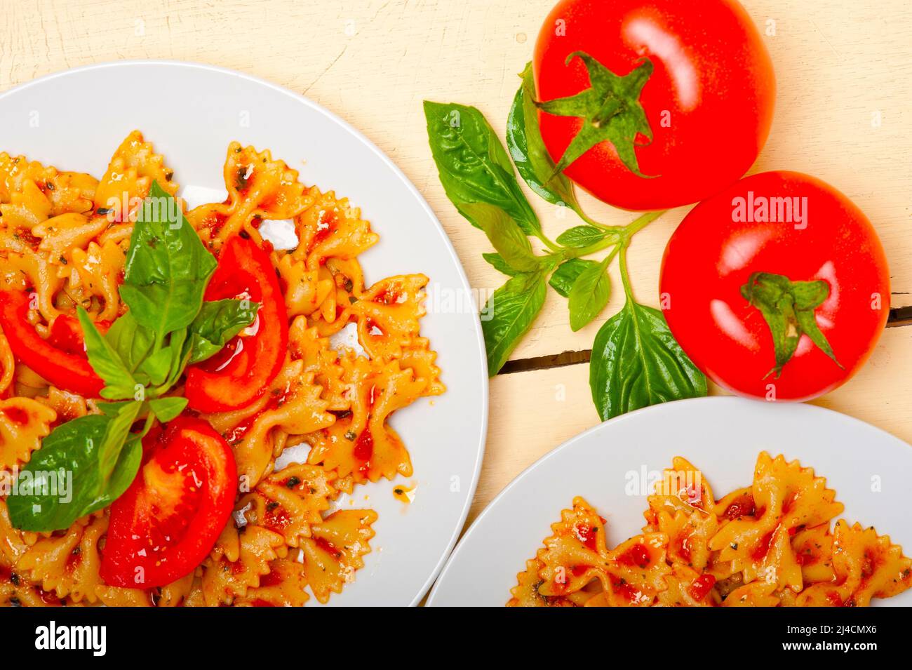 La pasta italiana Le farfalle butterfly bow tie-in pomodoro con salsa al basilico bianco su tavola in legno rustico Foto Stock