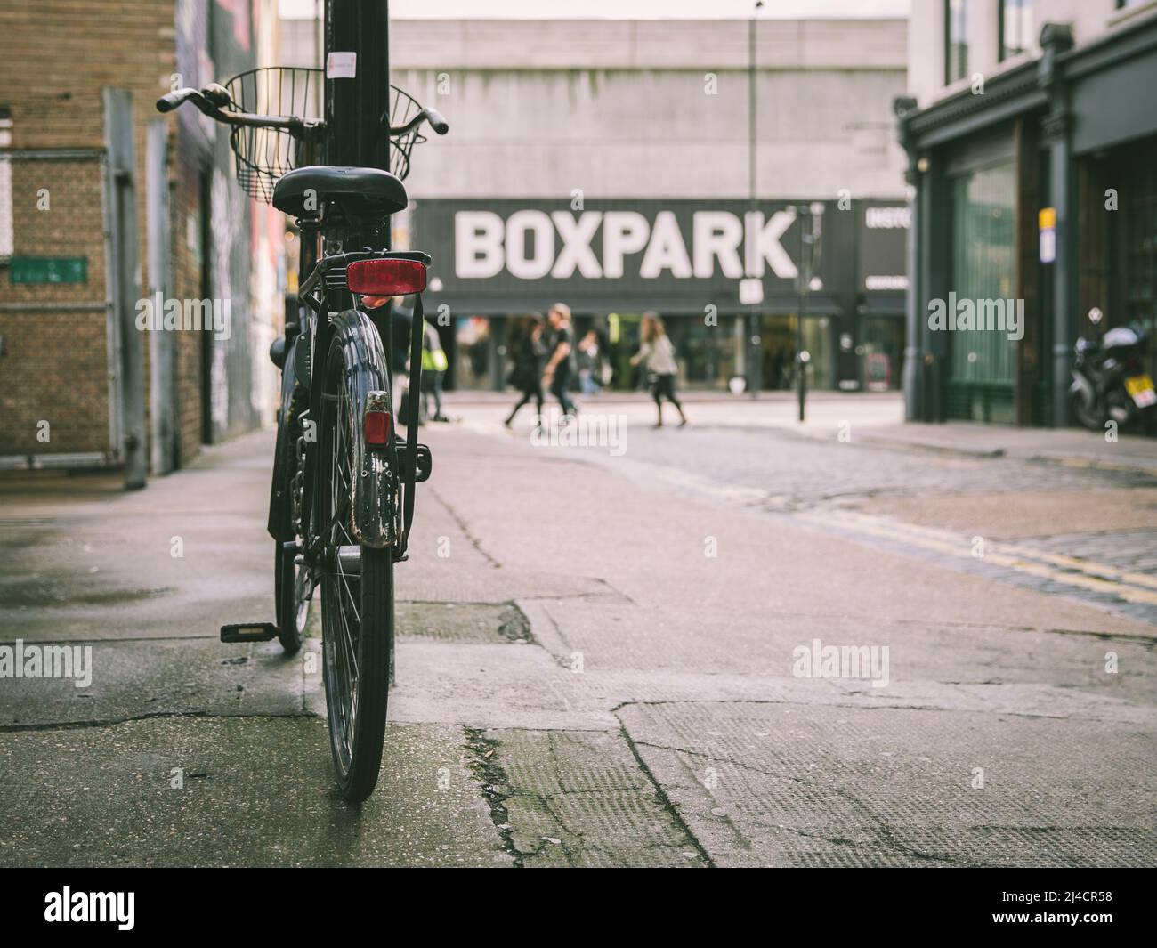 Shoreditch, Londra, Regno Unito - 14 aprile 2016: Una bicicletta stazionaria, con il centro commerciale Boxpark visibile sullo sfondo. Foto Stock