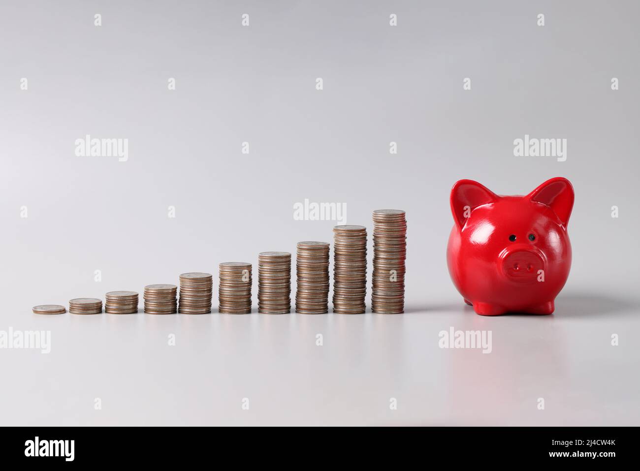 Pila di monete in ordine ascendente e red piggy banca su tavola, redditizio investimento di fondi Foto Stock