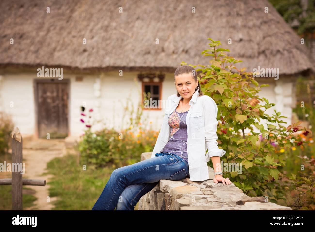 Giovane graziosa donna ucraina seduta vicino a casa di campagna rurale vecchia Foto Stock