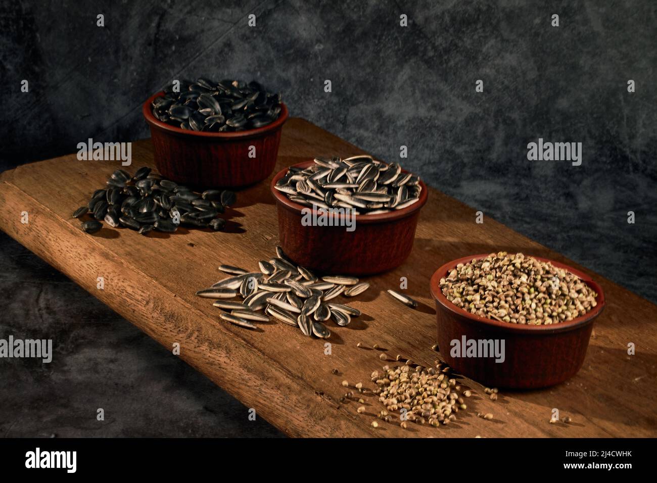 Tavola di grano. Due tipi di semi di girasole e semi di canapa medicinale in ciotole di ceramica su un asse di legno Foto Stock