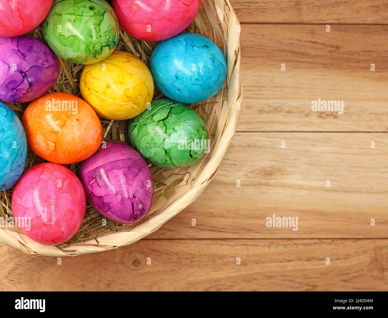 Vista dall'alto delle uova di pasqua colorate in cestino di paglia su sfondo di legno con spazio copia, Foto Stock