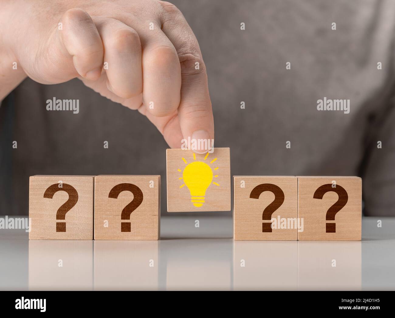 Idea creativa di concetto e innovazione. Blocco di cubo di legno selezionato a mano con lampadina. Simbolo del punto interrogativo e icona della lampadina Foto Stock