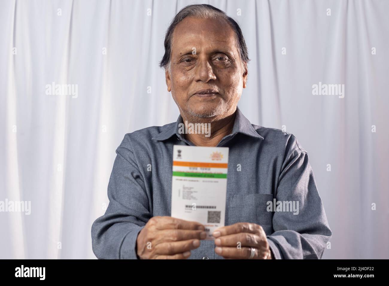 Un vecchio indiano sorridendo con carta Aadhaar in mani su sfondo bianco Foto Stock