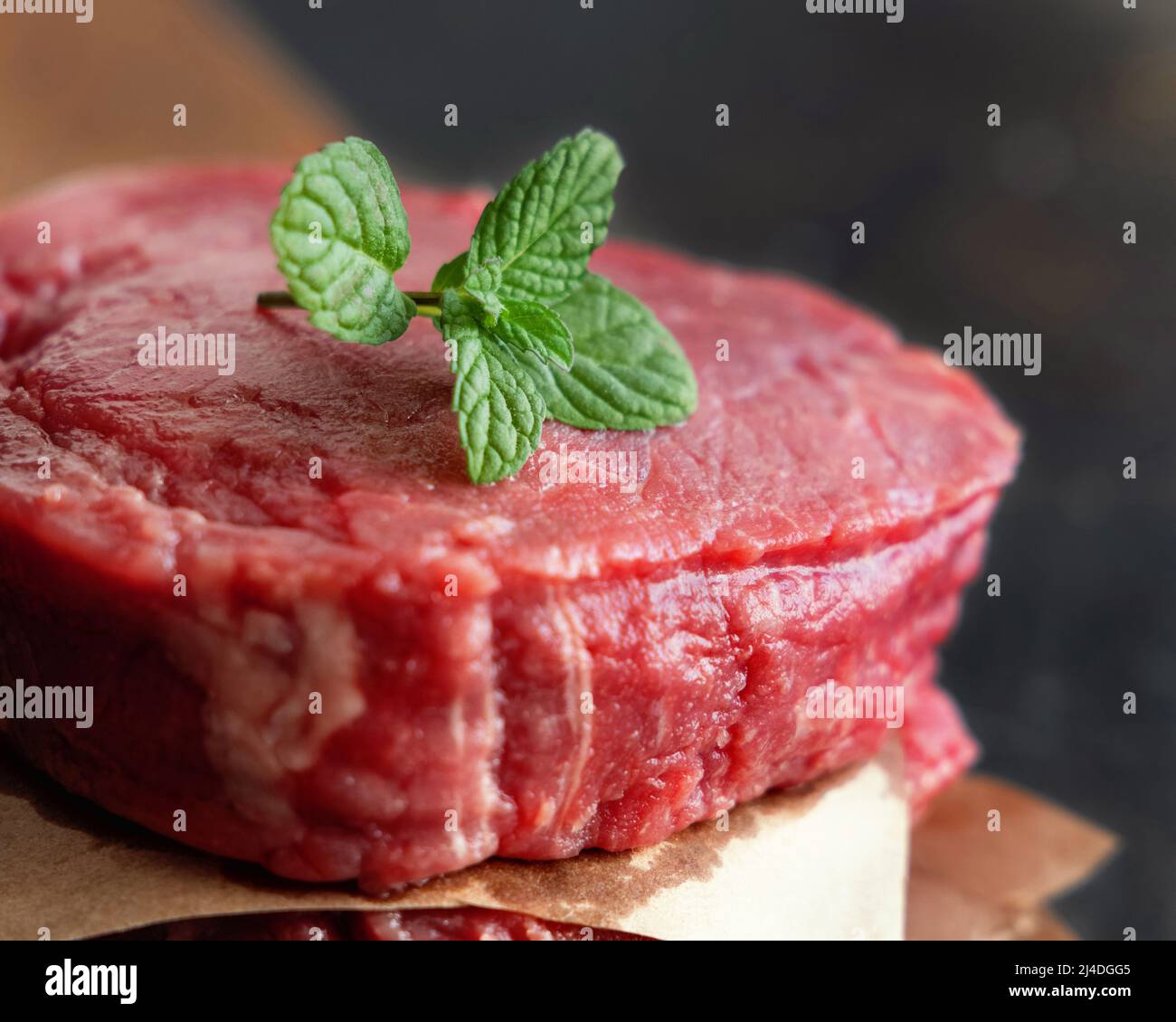 Bistecche di filetto di manzo crudo su tavola di legno su sfondo scuro da vicino. Meloni di filetto con spezie e ingredienti. Concetto di cibo estivo Foto Stock