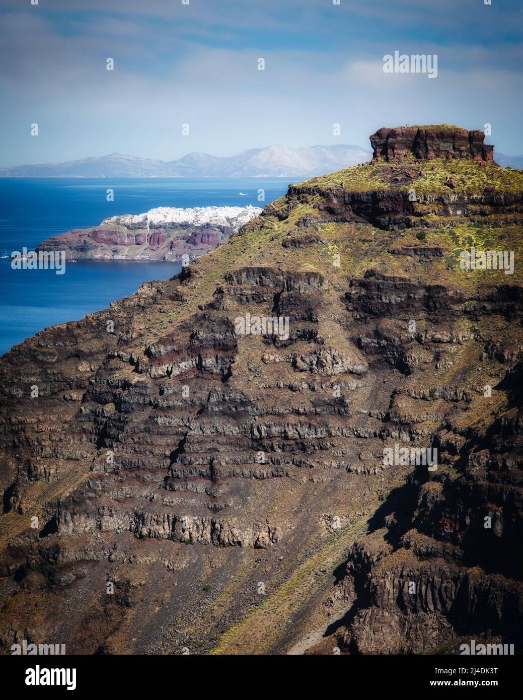 La roccia di Skaros nasconde parzialmente il lontano villaggio di Oia a Santorini, in Grecia. Foto Stock