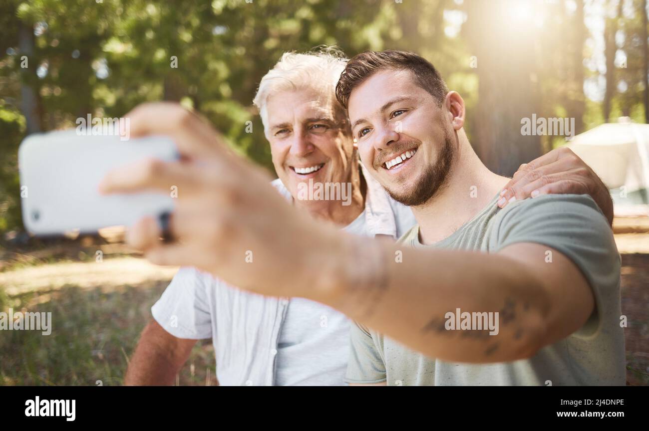 Sorridi. Scatto corto di un bel giovane uomo e suo padre che prende selfie mentre si accampano nei boschi. Foto Stock