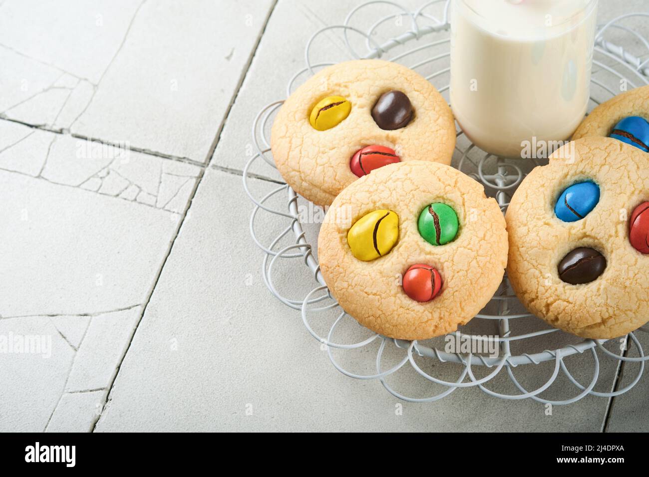 Biscotti fatti in casa con caramelle colorate al cioccolato e latte. Accatastate biscotti frollini con caramelle multicolore sul piatto con una bottiglia di latte accesa Foto Stock
