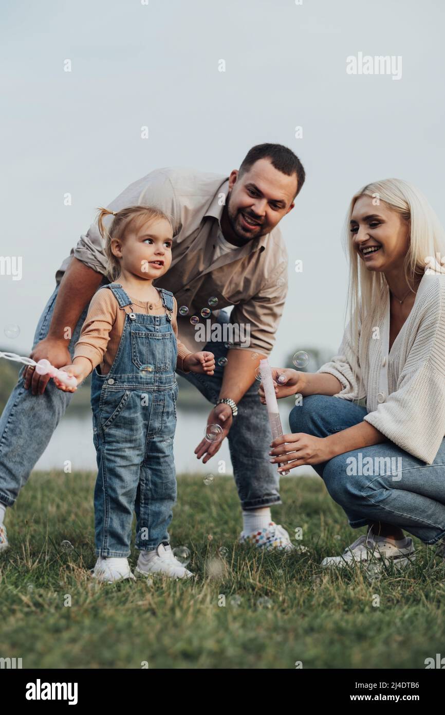 Ritratto di giovane felice famiglia, mamma e papà con la loro figlia che si divertono all'aperto fuori della città Foto Stock