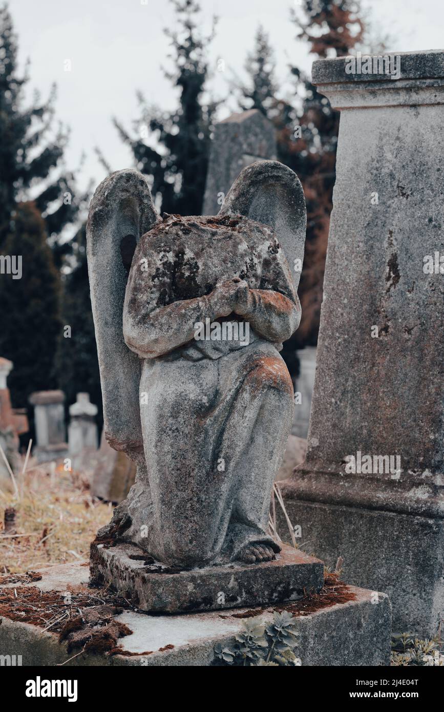 Lapide danneggiata, scultura di angelo di pietra decapitato nel cimitero antico abbandonato. Cimitero dimenticato, tomba sconosciuta. Messa a fuoco selettiva. Immagine verticale Foto Stock