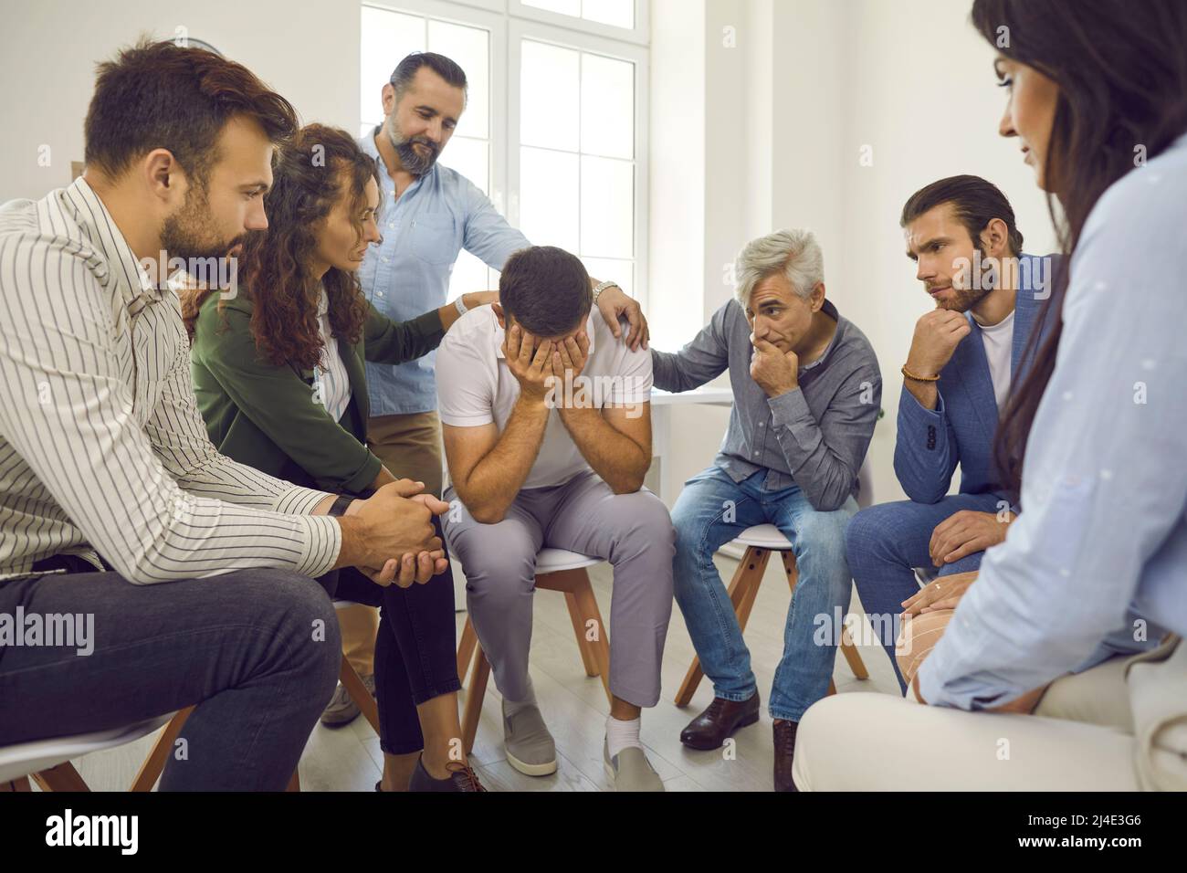Persone che sostengono e confortano un giovane che piange durante una sessione di terapia di gruppo Foto Stock