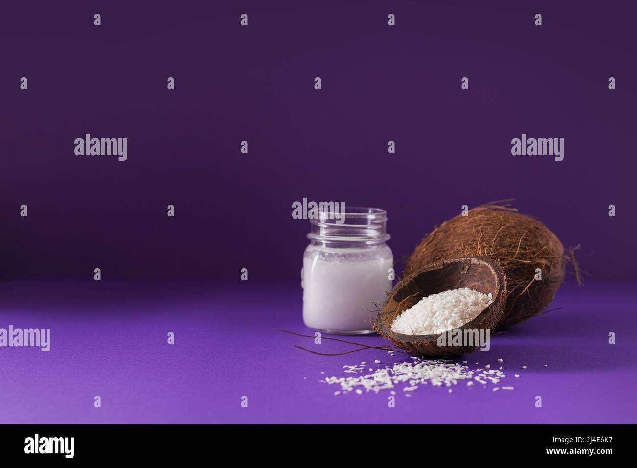 Cocco, fiocchi e olio di cocco in vaso su sfondo viola Foto Stock