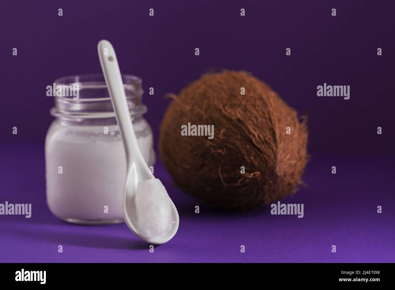 Cocco, fiocchi e olio di cocco in vaso su sfondo viola Foto Stock